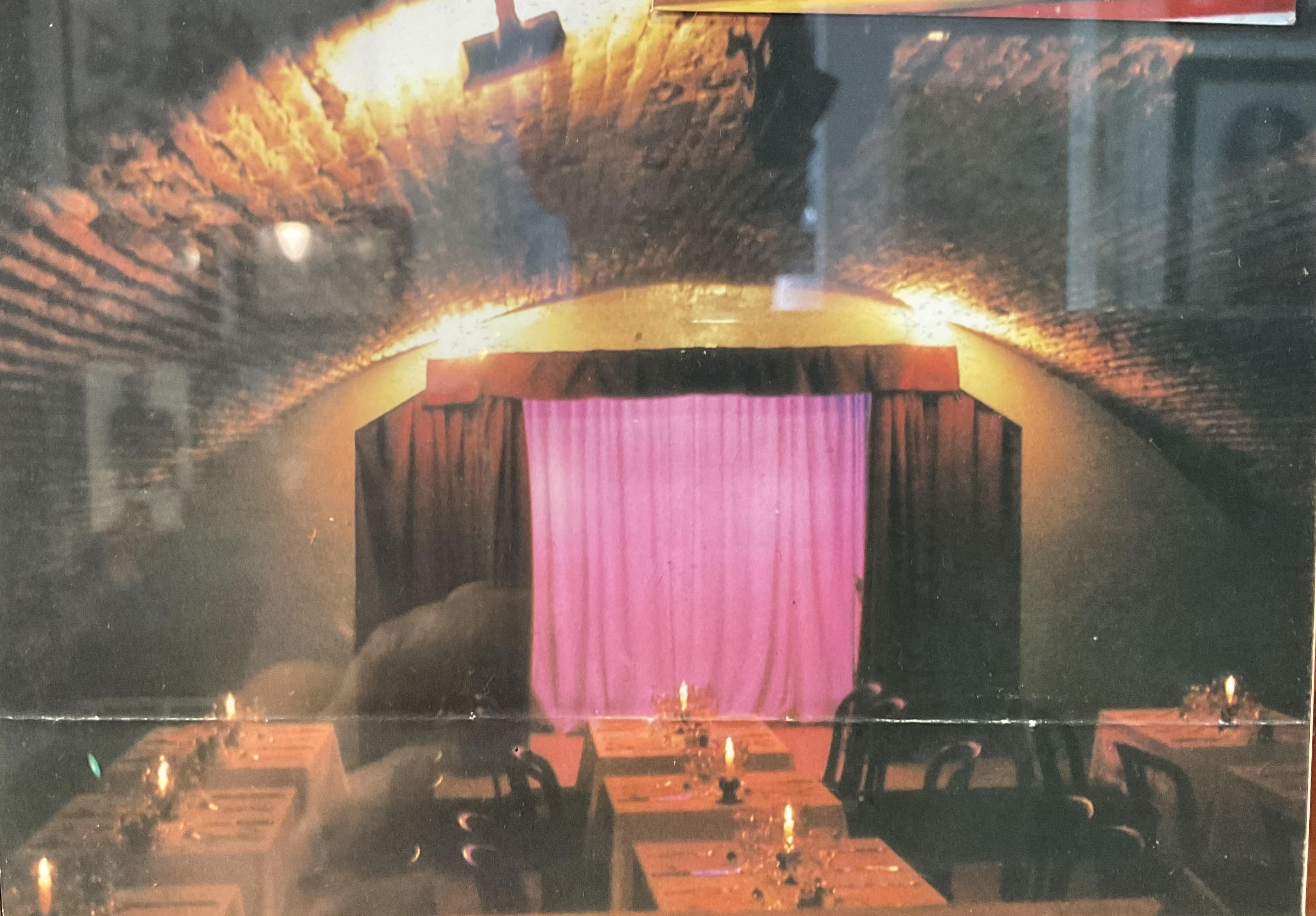 La salle du Citron Bleu en dîner-spectacle, tables dressées aux bougies sous les voûtes, rideau rose